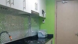 Une cuisine avec un plan de travail noir, un évier en acier inoxydable et un mur vert.