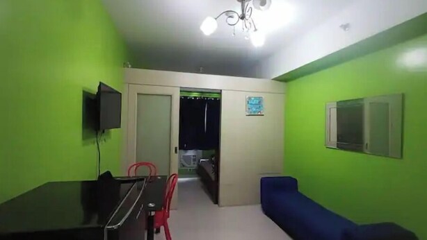 A room with green walls, a ceiling fan, a TV mounted on the wall, a dining table with chairs, and a blue sofa. - MOA VIEW 16TH flr unit (Pasay)