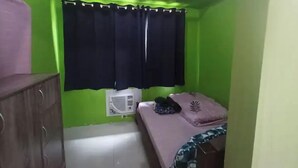 A small room with green walls, a bed with a patterned blanket, a wooden cabinet, and a window with black curtains. - MOA VIEW 16TH flr unit (Pasay)