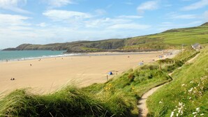 A beach with a path leading to a grassy area, a sandy beach, and a view of the sea and hills in the distance. - 3 bedroom accommodation in St Davids (St Davids)