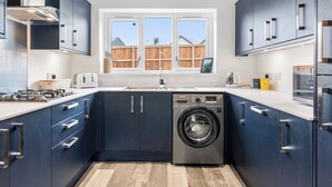 A modern kitchen with a built-in washer, a window, and a view of a wooden fence. - 3 bedroom accommodation in St Davids (St Davids)