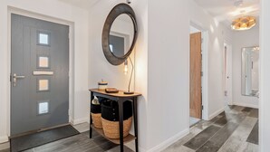 A modern hallway with a grey door, a round mirror, a small console table with baskets, and a light fixture. - 3 bedroom accommodation in St Davids (St Davids)