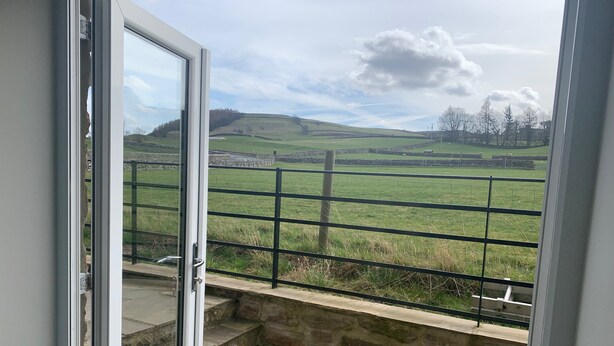 A view from a balcony with stone steps leading to a metal railing overlooking a green field and distant hills. - White Lea is a beautiful Dales Cottage recently transformed into a fantastic holiday home. (Richmond)