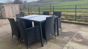 An outdoor patio with a table and chairs, a wooden shed, and a view of green fields and hills. - White Lea is a beautiful Dales Cottage recently transformed into a fantastic holiday home. (Richmond)