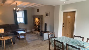 A cozy living room with a stone fireplace, a sofa, a dining table with chairs, and a chandelier. - White Lea is a beautiful Dales Cottage recently transformed into a fantastic holiday home. (Richmond)