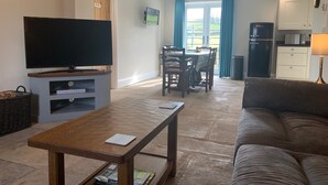 A living room with a television, a coffee table, a sofa, a dining area with a table and chairs, and a kitchen area with cabinets and a refrigerator. - White Lea is a beautiful Dales Cottage recently transformed into a fantastic holiday home. (Richmond)