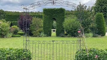 A metal gate with an arch design, surrounded by well-manicured hedges and a lawn.