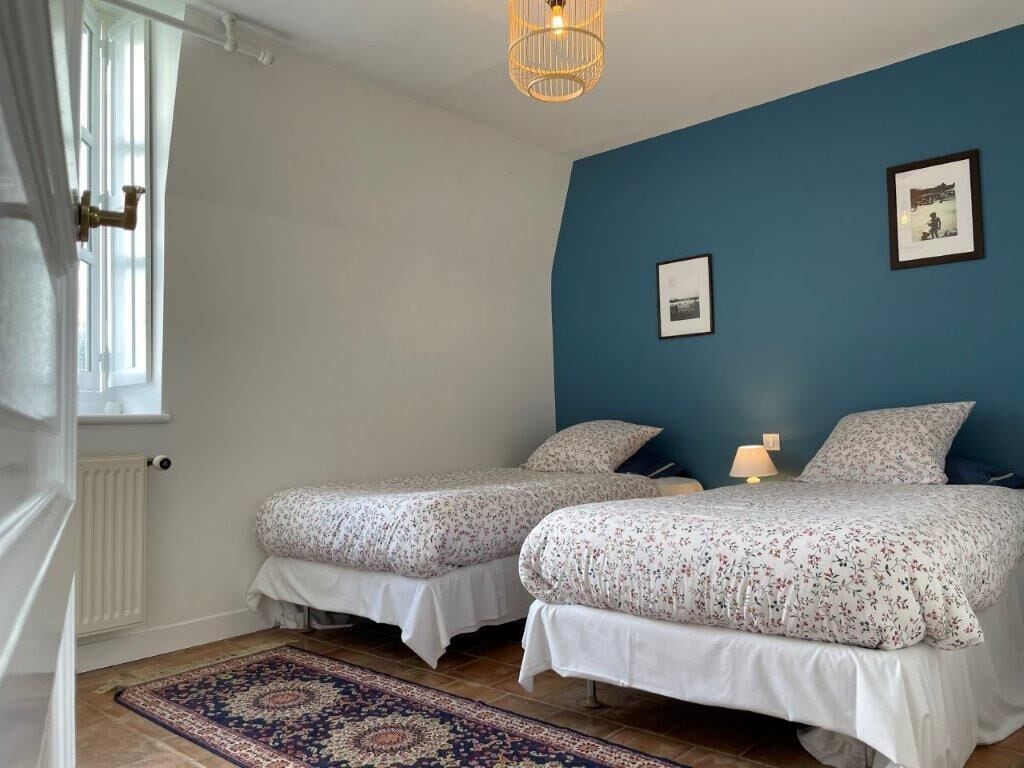 Un dormitorio con dos camas, una pared azul, un cuadro enmarcado y una alfombra estampada.