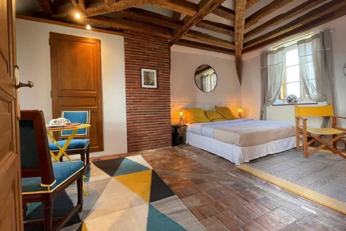 Un dormitorio con cama, escritorio, silla, espejo y ventana con cortinas.