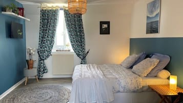 Ein Schlafzimmer mit Bett, Nachttisch mit Lampe, Fenster mit Vorhängen und einer Wandablage mit Pflanzen.