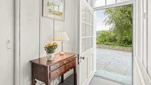 Eine weiße Tür mit Glasfenster, ein Holzkonsolentisch mit Lampe und Blumen, und ein gerahmtes Bild an der Wand.