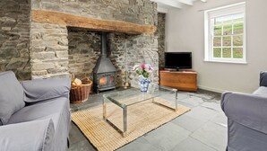 Ein Wohnzimmer mit Kamin aus Stein, einem Fernseher und Blick ins Freie durch ein Fenster.
