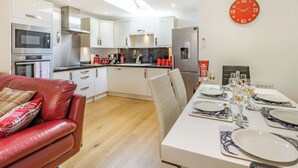 Una cucina moderna con zona pranzo, che include un divano in pelle rossa, un tavolo da pranzo bianco e un orologio rosso appeso al muro.