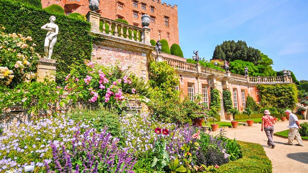 A historic building with a large garden, statues, and a well-maintained lawn.