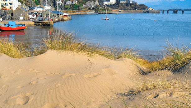 Eine Küstenlandschaft mit Sandstrand, Booten und Häusern an einem Hügelhang.
