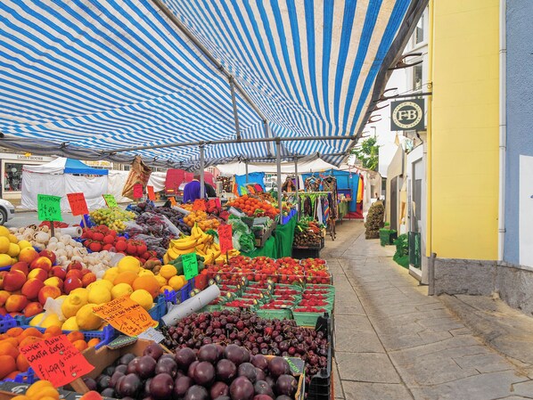 A market with various fruits and vegetables displayed under striped canopies.