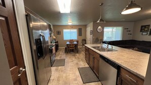 A modern kitchen with stainless steel appliances, a large island with a sink, wooden cabinets, and a dining area with a table and chairs.
