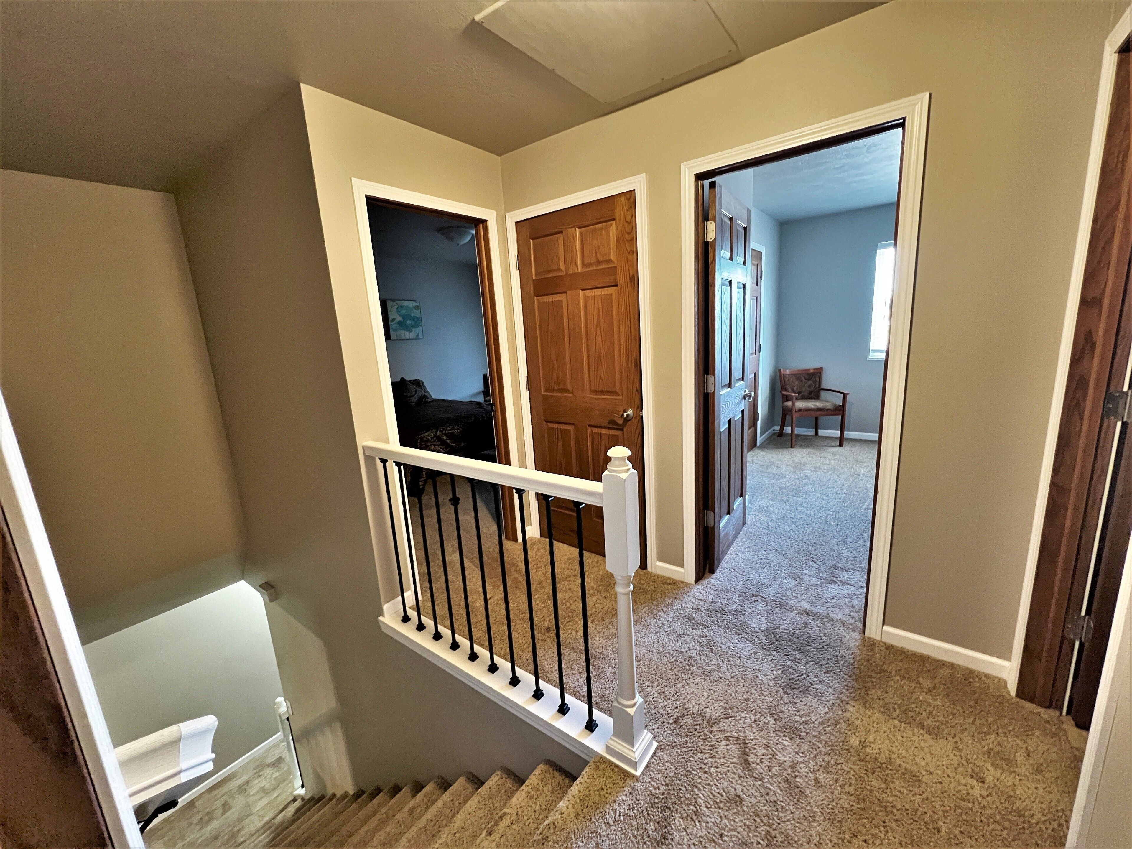 A staircase with a white railing leading to a bedroom with a dark-colored bed and a painting on the wall.