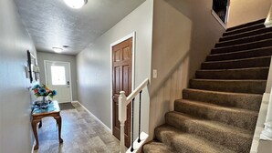 A hallway with a wooden door, a small table with a vase, and a carpeted staircase.