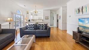 Ein geräumiges Wohnzimmer mit grauem Sofa, einem Glastisch und einem Fernseher auf einem Holzständer.