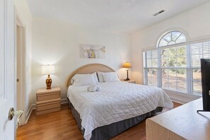 Une chambre à coucher avec un lit, des tables de chevet, une lampe, un téléviseur et une fenêtre avec des stores.