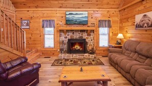 A cozy log cabin interior with a stone fireplace, leather sofas, and a wooden table. - 3 Kings / Deck / Fireplace / 100Mbps / Games Games/ Parking/ Dollywood 5mi (Sevierville)