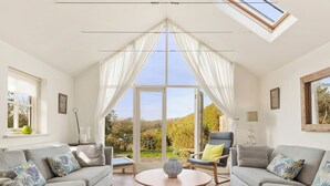 A spacious living room with two sofas, a coffee table, and a view of a garden through large windows. - 4 bedroom accommodation in Manorbier (Manorbier)
