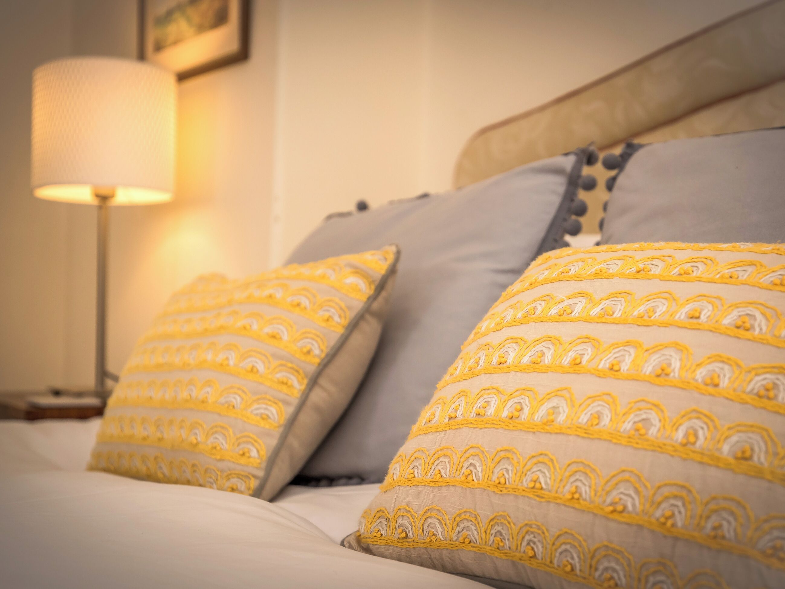 Un lit avec deux oreillers à motifs jaunes et blancs, une lampe de chevet et une tête de lit en bois.