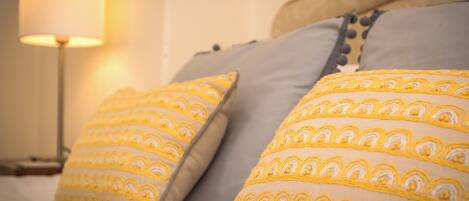 Un lit avec deux oreillers à motifs jaunes et blancs, une lampe de chevet et une tête de lit en bois.