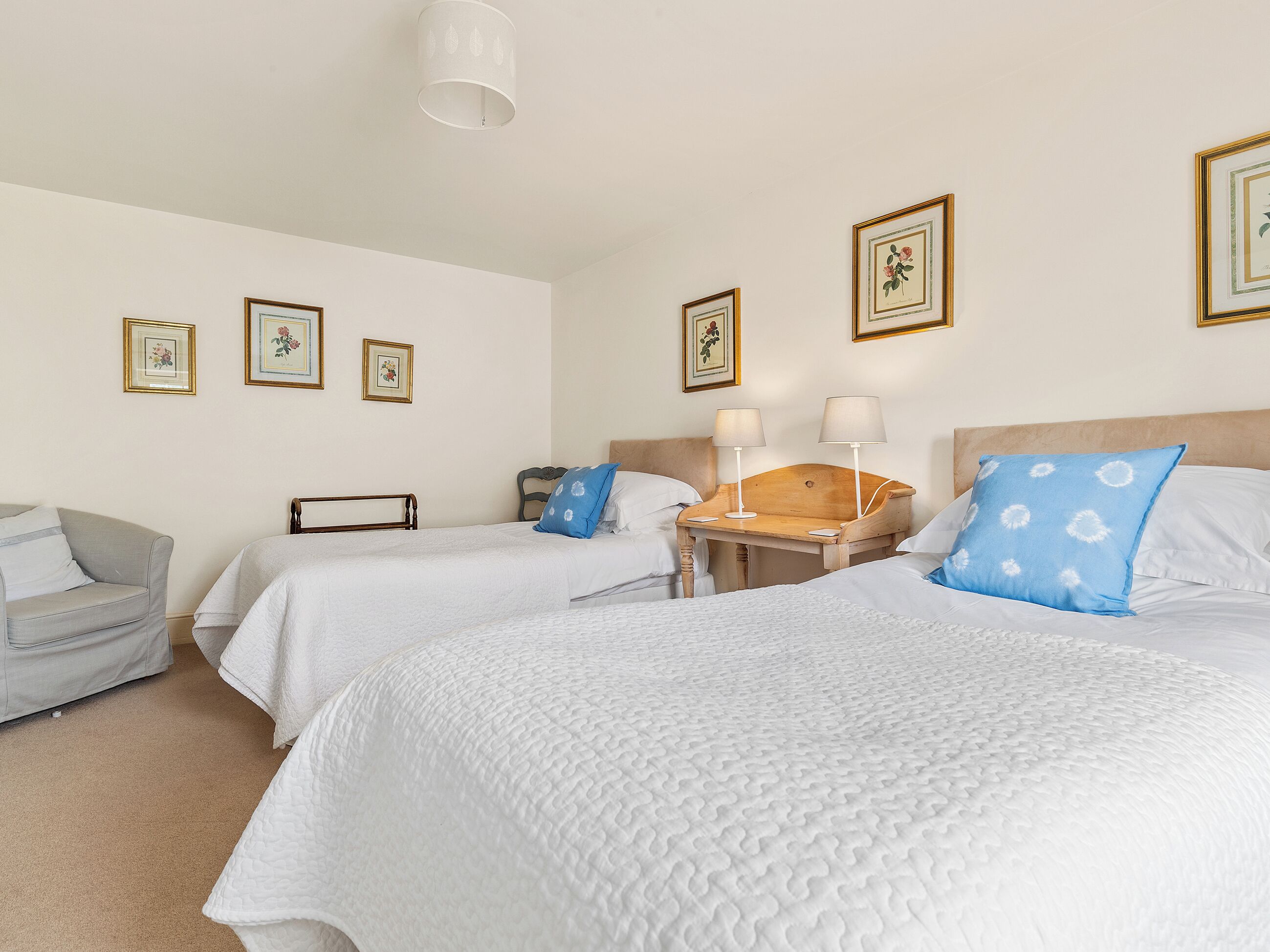 Een hotelkamer met twee bedden, een houten nachtkastje, een stoel en ingelijste foto’s aan de muur.