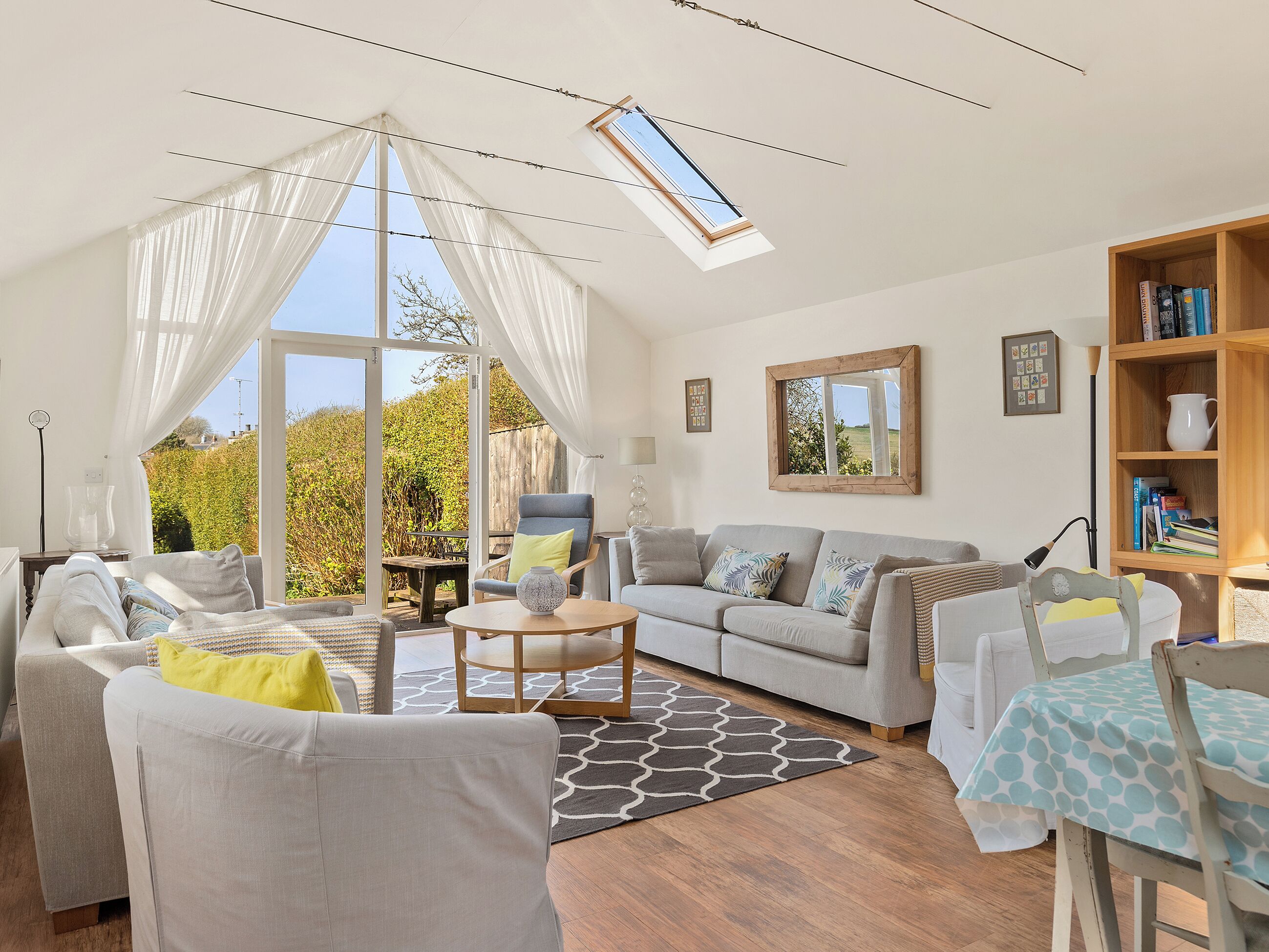 A spacious living room with a large window, a wooden ceiling, and a bookshelf.