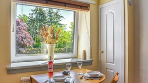 Une table à manger ornée d’un vase de fleurs séchées, d’une bouteille de vin et d’un verre de vin.