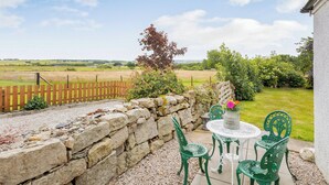 Une terrasse avec un mur en pierre, une table ronde et deux chaises.