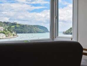 Blick aus einem Fenster auf eine Küstenlandschaft mit Booten, Grünpflanzen und Gebäuden.