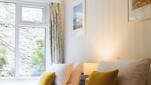 Un dormitorio con cama, almohadas, mesita de noche, lámpara y ventana con cortinas.