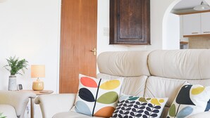 Una sala de estar con un sofá color beige, cojines coloridos, una puerta de madera y un mueble de madera oscura.