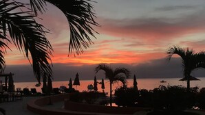Ein Resort mit Poolbereich, Palmen und Blick auf das Meer bei Sonnenuntergang.