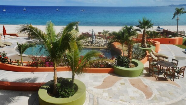 Poolbereich eines Resorts mit Blick auf das Meer, umgeben von Palmen und Liegestühlen.