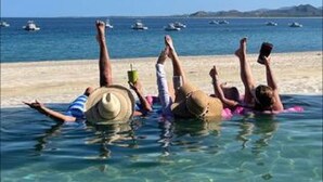 Drei Personen liegen am Strand mit den Füßen im Wasser, umgeben von Booten.