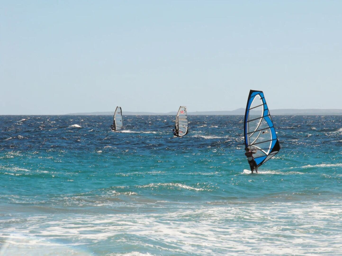 A beach with clear blue water and people windsurfing.