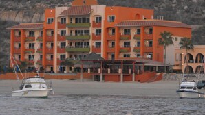 Ein mehrstöckiges Hotel mit Balkonen, einer Strandlage und Booten auf dem Wasser.