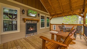 A wooden deck with a fireplace, outdoor seating, and large windows overlooking a forest. - Smoky Mountain Plunge (Gatlinburg)