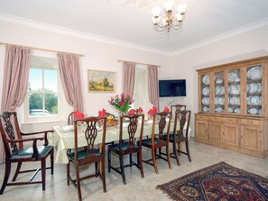 A dining room with a table set for six, wooden chairs, a chandelier, a television on the wall, and a cabinet with glass doors.