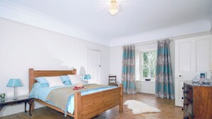 Een slaapkamer met een houten bed, twee nachtkastjes met lampen, een dressoir en een raam met gordijnen.