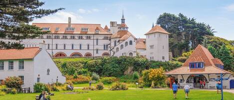 A historic building with a tower, surrounded by a well-maintained garden with benches and picnic tables.