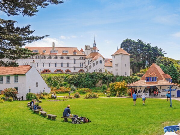 A historic building with a tower, surrounded by a well-maintained garden with benches and picnic tables.