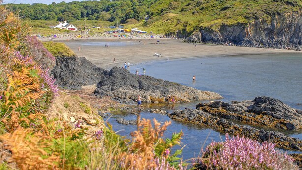 Una playa costera con costas rocosas, una playa de arena y colinas al fondo.