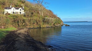 Una casa frente al mar con vista al océano y un faro a lo lejos.