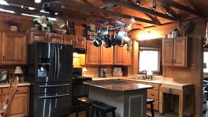 A rustic kitchen with wooden cabinets, a stainless steel refrigerator, and a hanging pot rack.