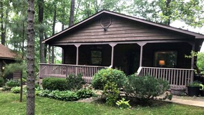 A wooden house with a porch, surrounded by a well-maintained lawn and various shrubs.